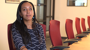 Haben Girma, wearing a patterned blue dress, smiles and sits at an office conference table.