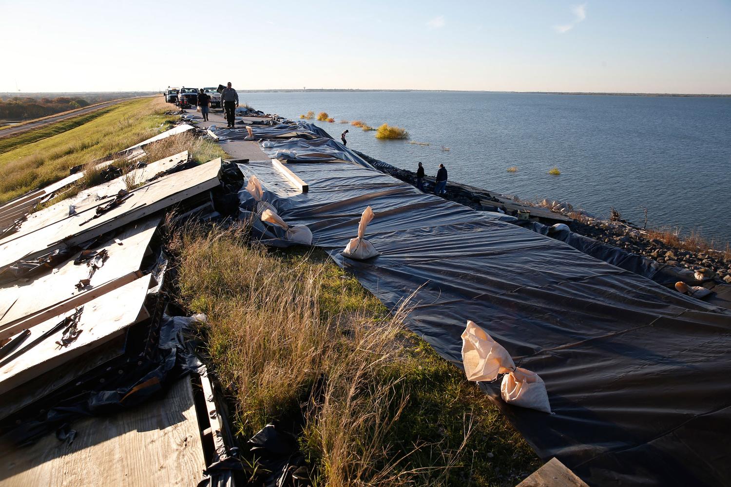 Workers deploy sandbags and tarps to temporarily prevent further erosion along a 160-foot-long slide in the Lewisville Dam. Corps engineers say the embankment is more unstable since the May flood because cracks have spread along the 20-foot-wide crest of the dam.