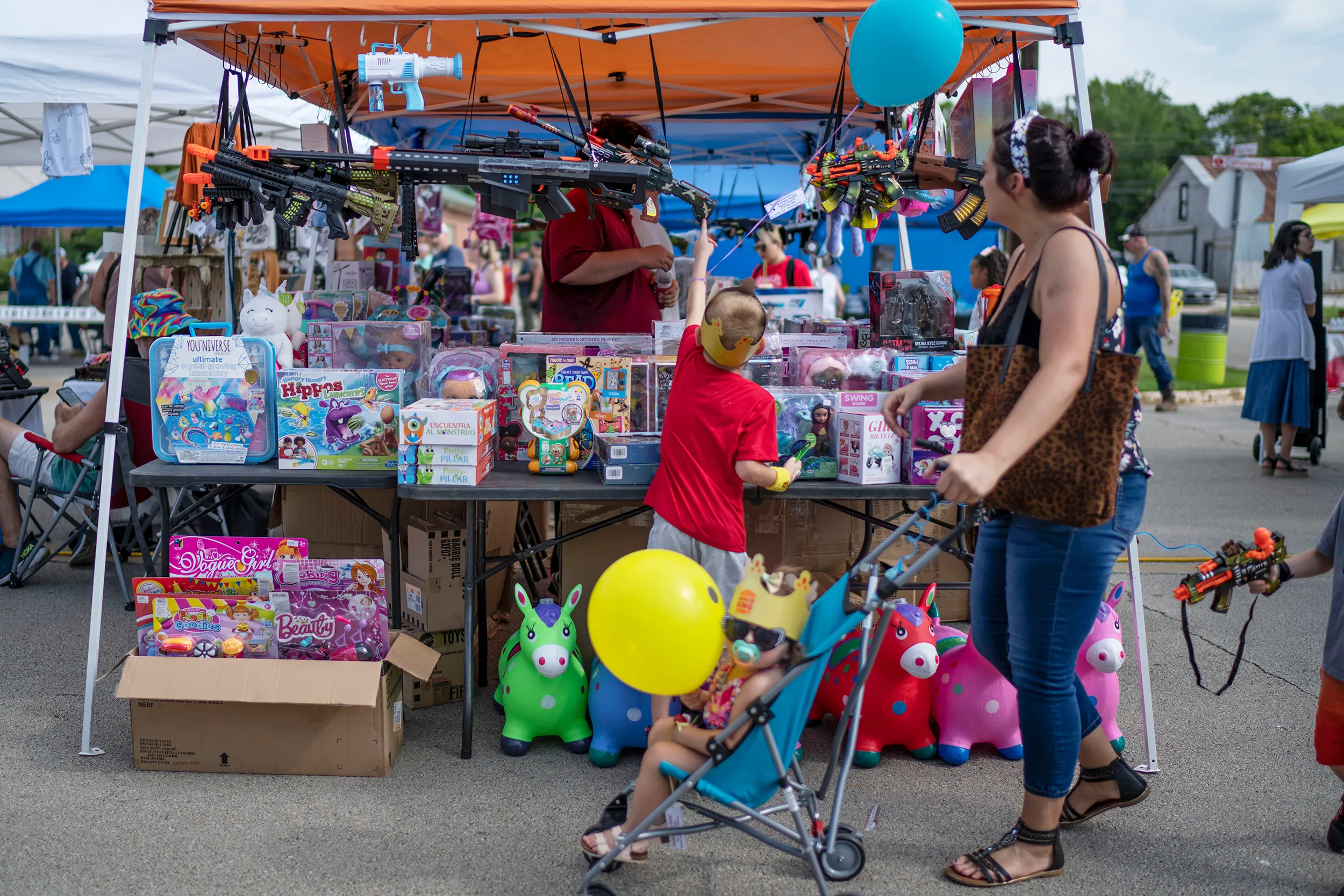 A fair stall with toys and a boy reaching for a toy machinegun.