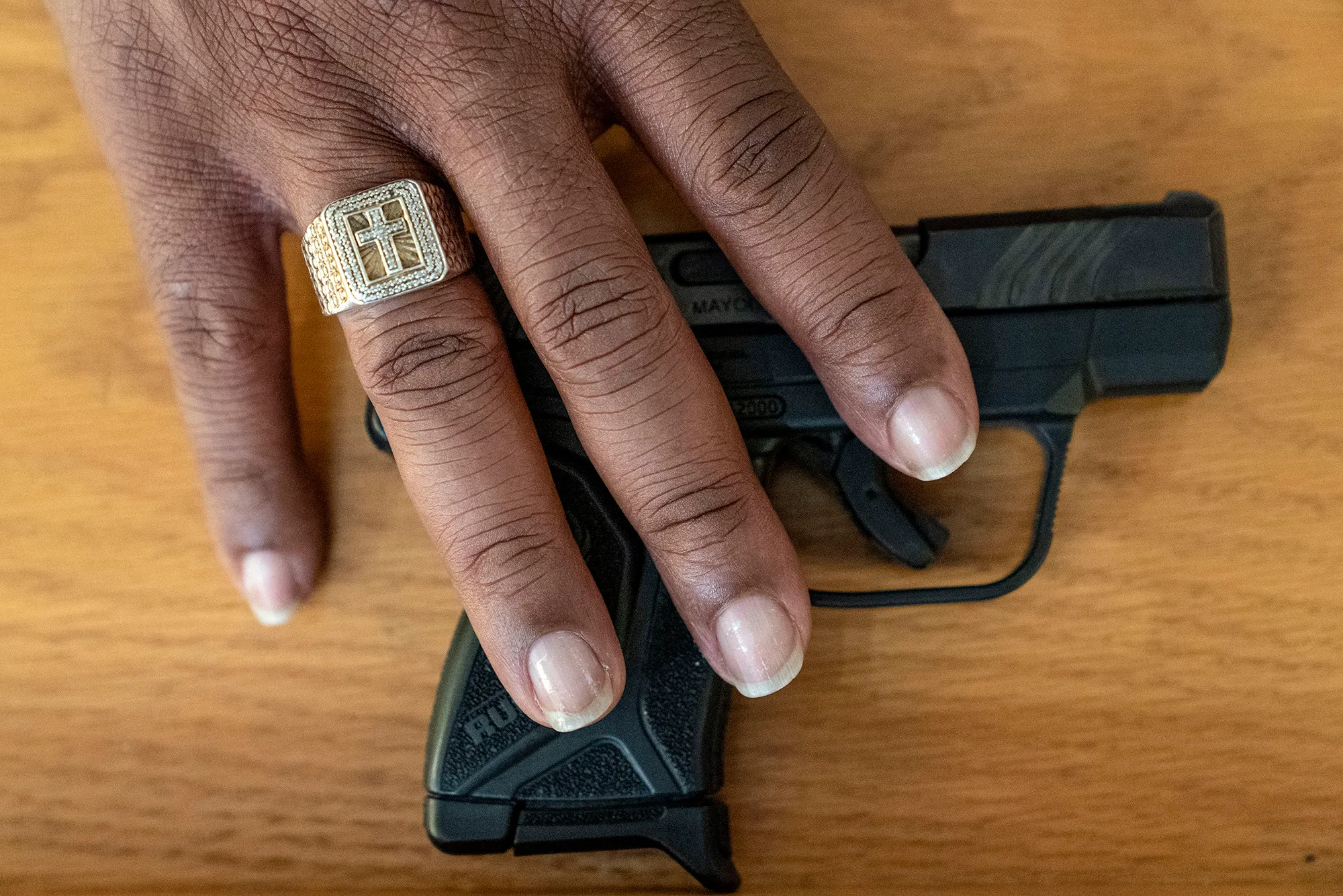 A mans hand wearing a gold ring with a crucifix over a gun.