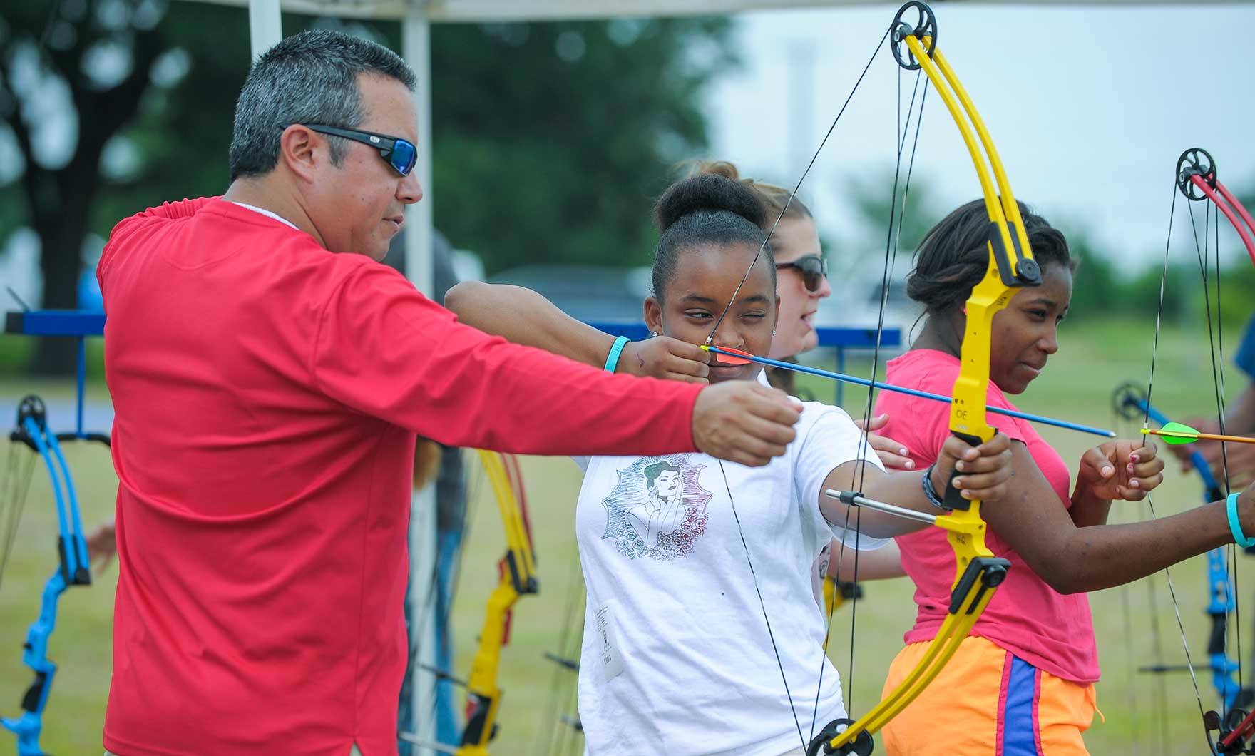 Instructor teaching archery to girls