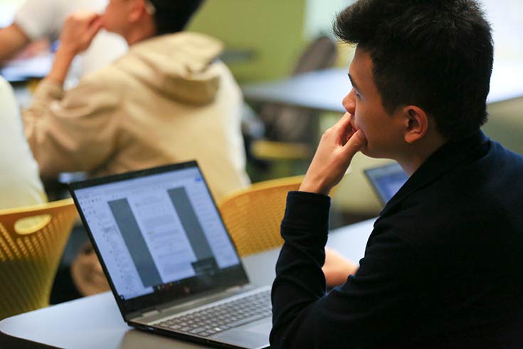 young man sitting at his laptop, looking to the front of the class