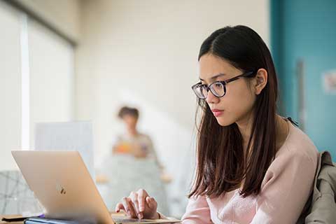 a student wearing glasses looks a laptop