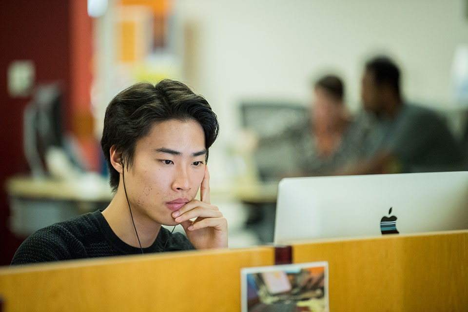 A student wearing headphones works on a computer