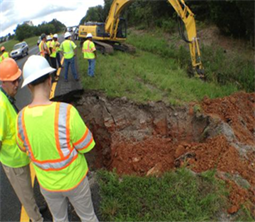 Photograph of a road destroyed by a sinkhole with an excavator in the background.