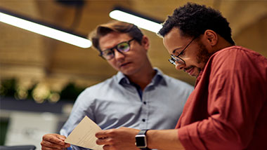 Two people with glasses reading a document together at a scientific conference.