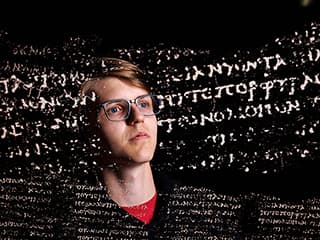 White Greek letters overlay Luke Farritor's face on a black background.