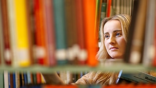 Student pulls books off a shelf in the Architecture Library.